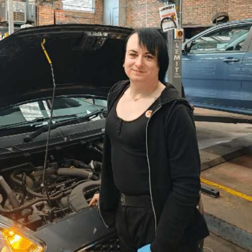 Transgender Vehicle Technician shares her experience of working in the automotive aftermarket while standing in front of an open car engine bonnet
